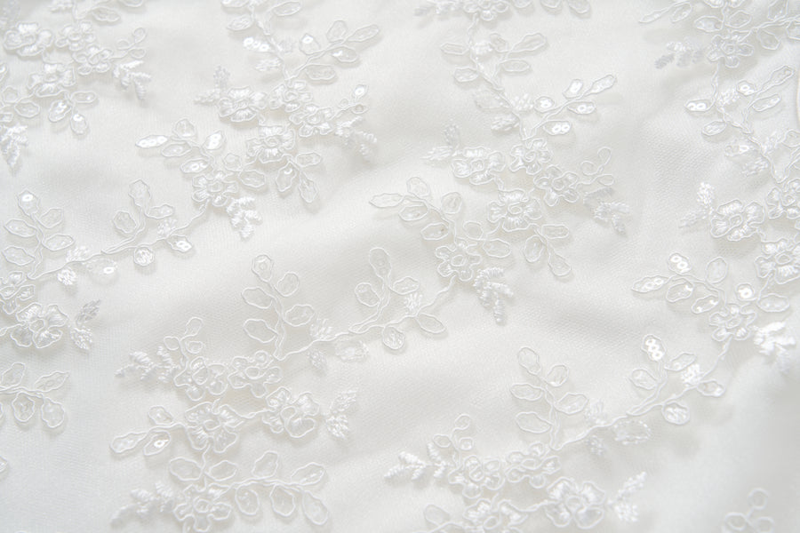 Close-up of the Twinkle Whisper Dress by KIKI and JOJO, featuring white lace fabric with floral embroidery and delicate sequins—ideal for anyone who loves an elegant embroidered lace or soft floral pattern look.