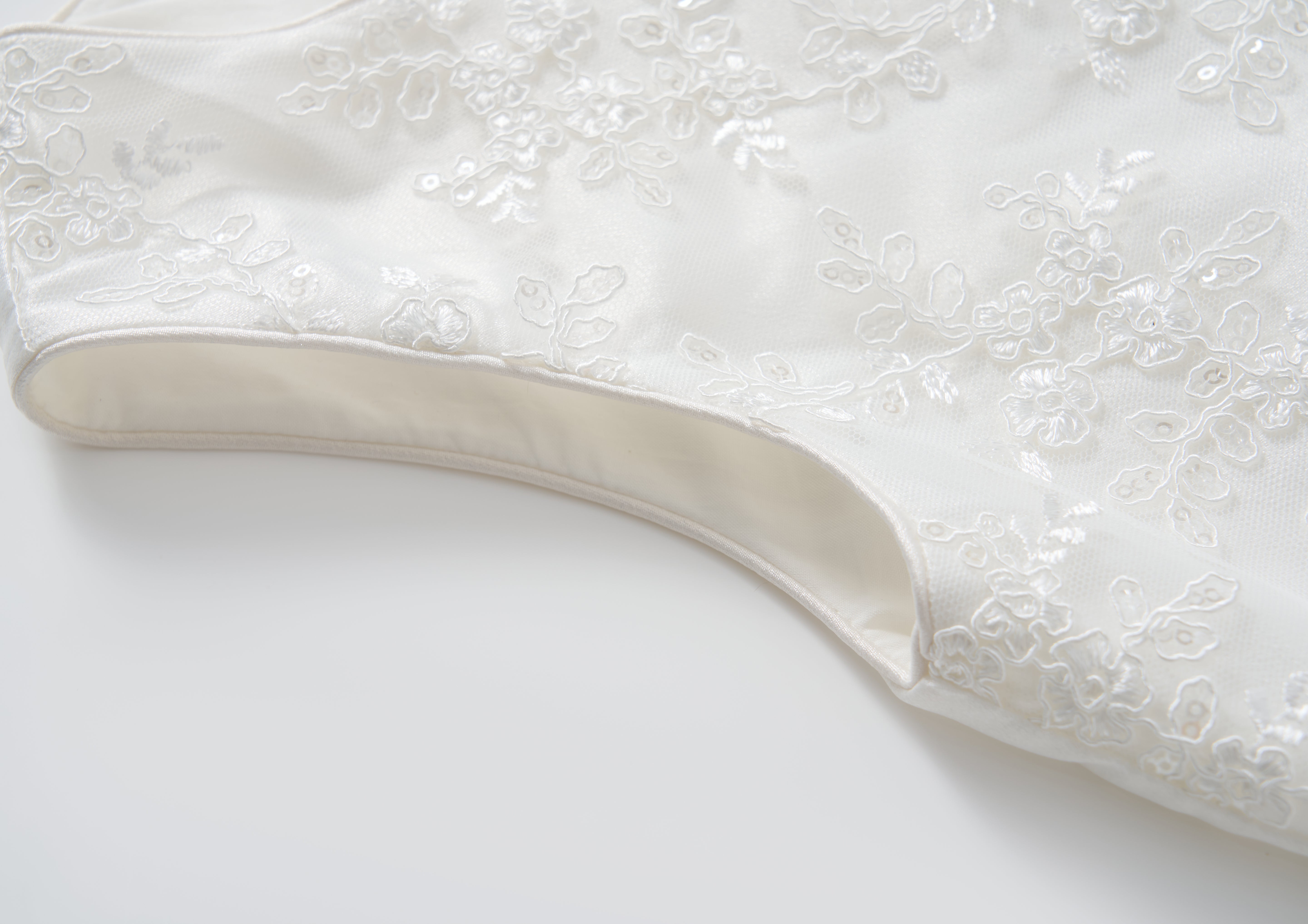 Close-up of the Twinkle Whisper Dress by KIKI and JOJO, a white A-line style featuring floral embroidery, laid flat on a light surface.