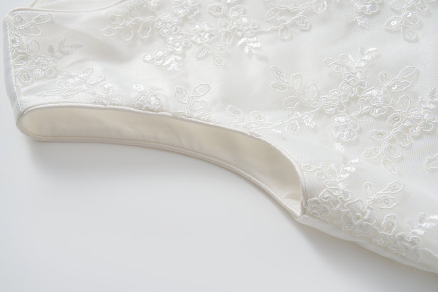 Close-up of the Twinkle Whisper Dress by KIKI and JOJO, a white A-line style featuring floral embroidery, laid flat on a light surface.