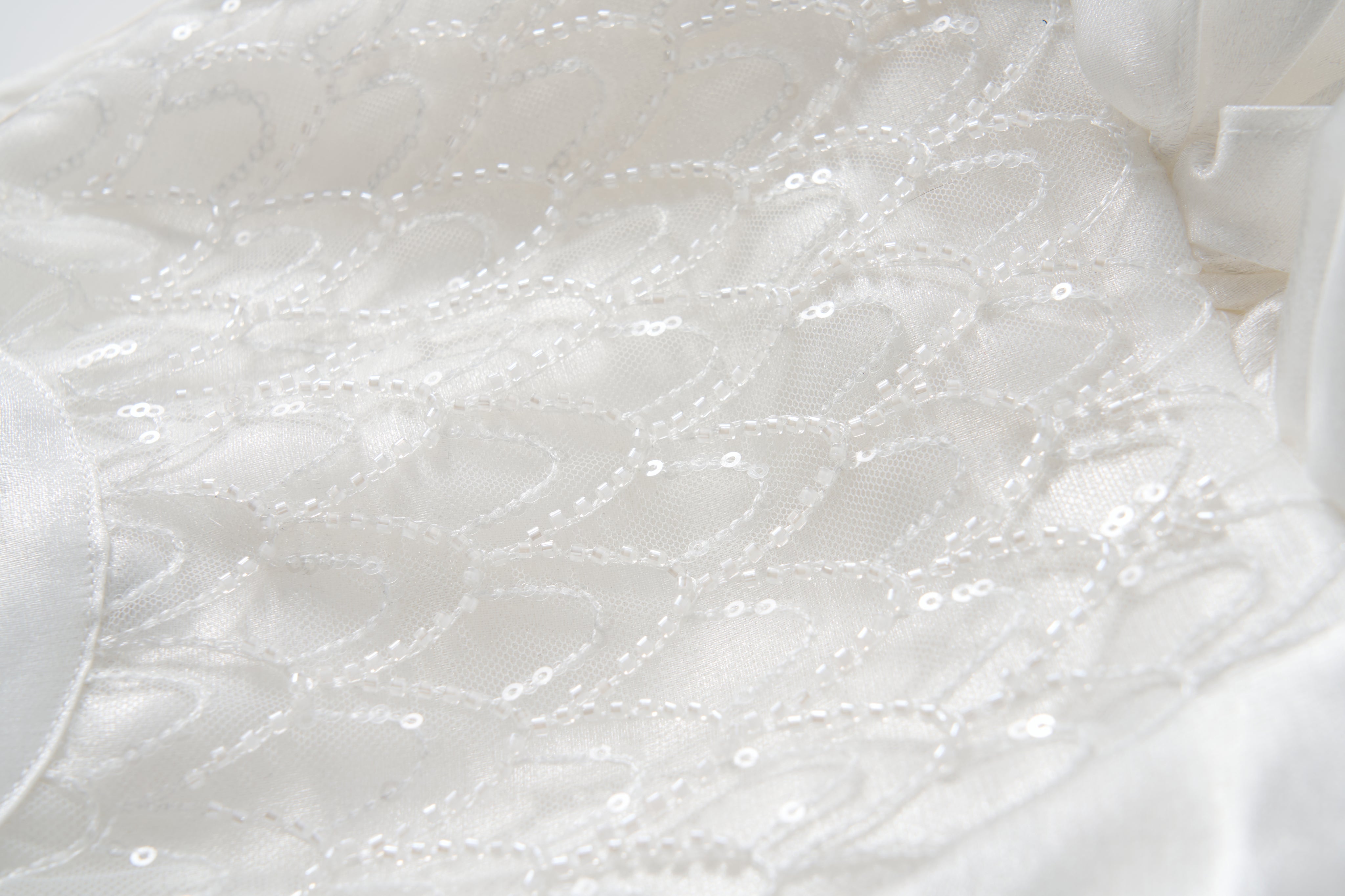 Close-up of the Pearl Glow Whisper Dress by KIKI and JOJO, featuring white fabric with geometric stitching, beaded embroidery, and sparkling sequins—ideal for a princess-style A-line look.