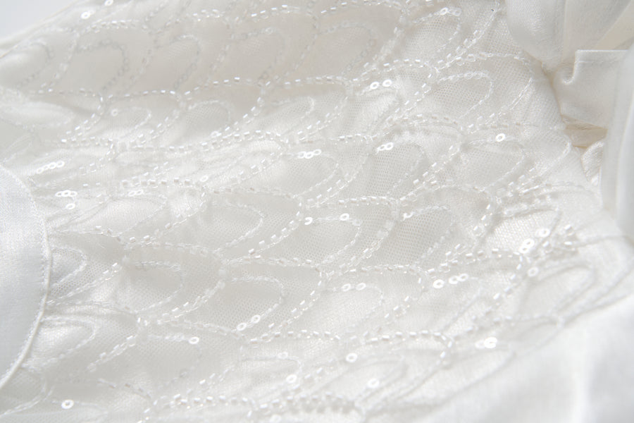 Close-up of the Pearl Glow Whisper Dress by KIKI and JOJO, featuring white fabric with geometric stitching, beaded embroidery, and sparkling sequins—ideal for a princess-style A-line look.