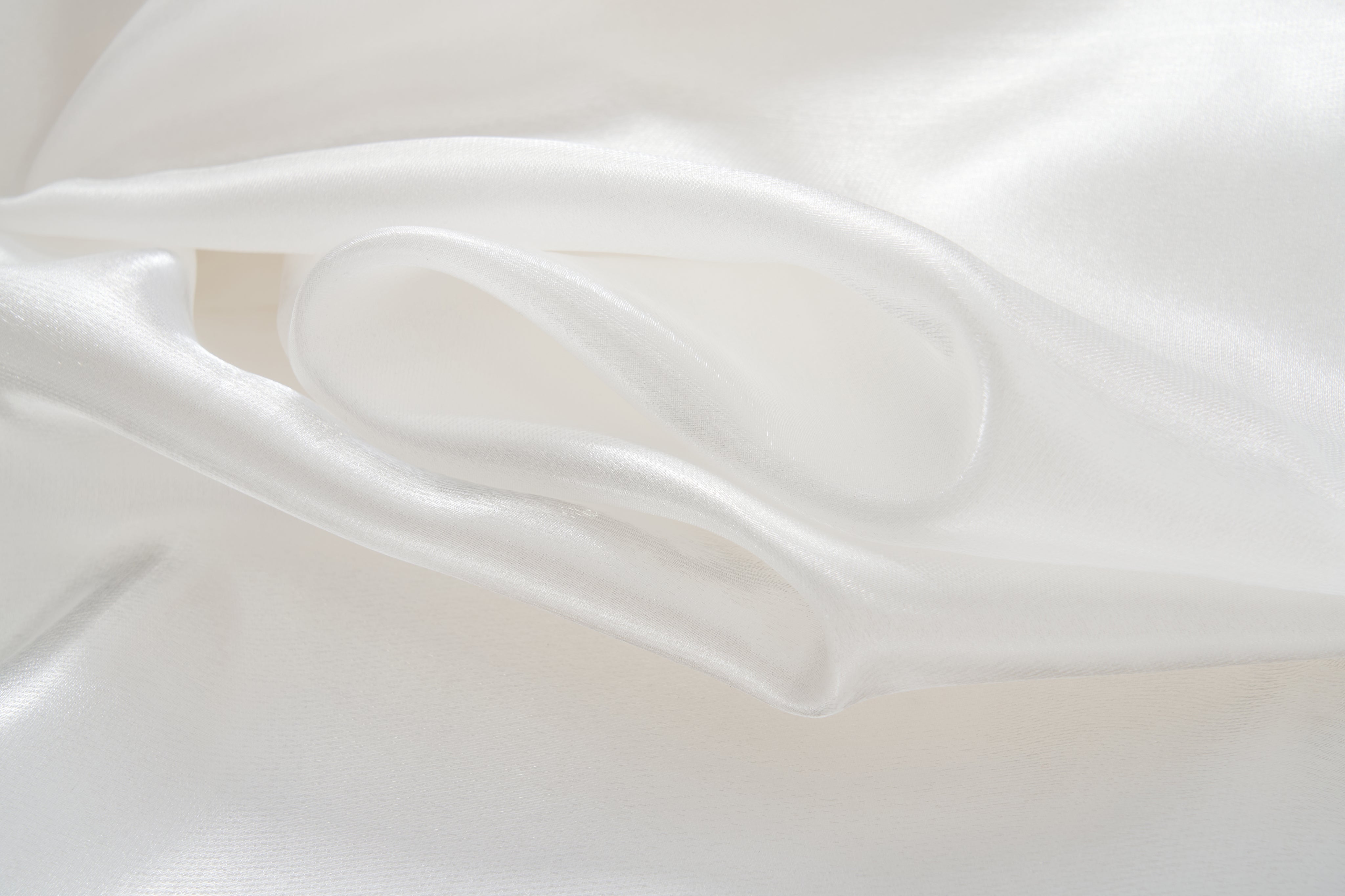 Close-up of the smooth, white silk fabric of the KIKI and JOJO Pearl Glow Whisper Dress, featuring gentle folds and a soft sheen that evoke the elegance of delicate beaded embroidery.
