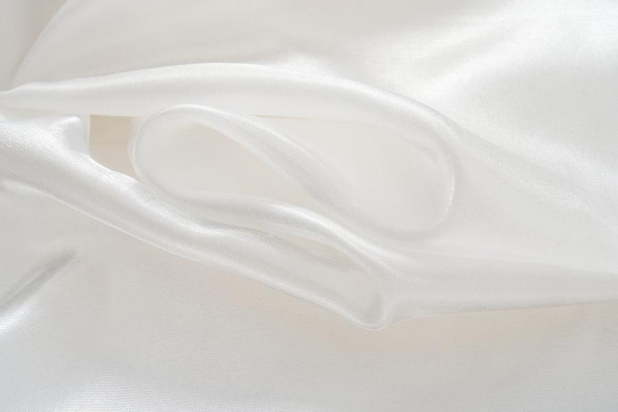 Close-up of the smooth, white silk fabric of the KIKI and JOJO Pearl Glow Whisper Dress, featuring gentle folds and a soft sheen that evoke the elegance of delicate beaded embroidery.