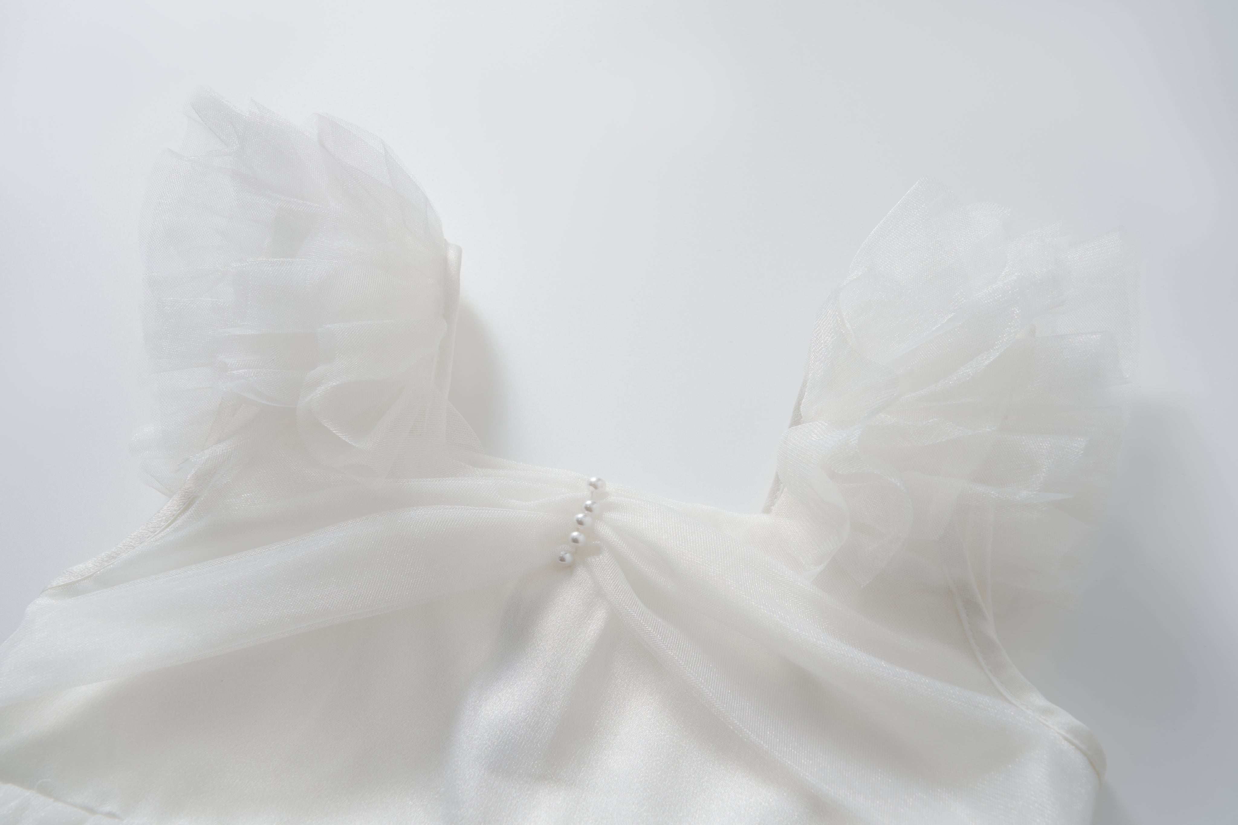 The Cloud Whisper Dress by KIKI and JOJO features sheer, ruffled tulle sleeves and a row of small pearls on the chest, shown on a plain white background.