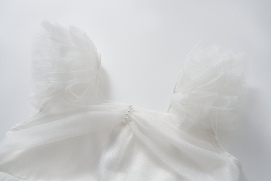 The Cloud Whisper Dress by KIKI and JOJO features sheer, ruffled tulle sleeves and a row of small pearls on the chest, shown on a plain white background.