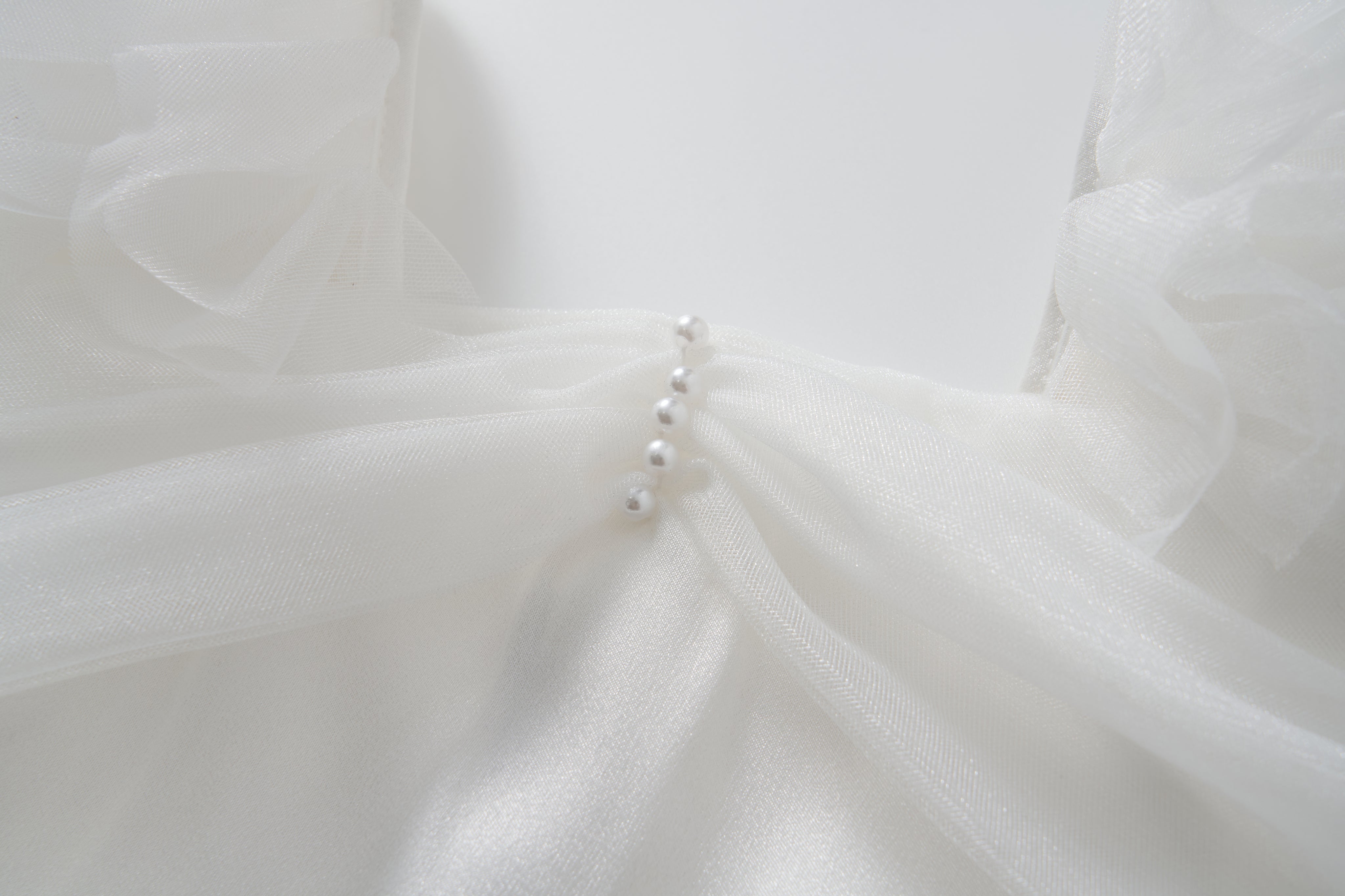 Close-up of the Cloud Whisper Dress by KIKI and JOJO, showcasing sheer white tulle and five pearl-like buttons arranged vertically at the center front.