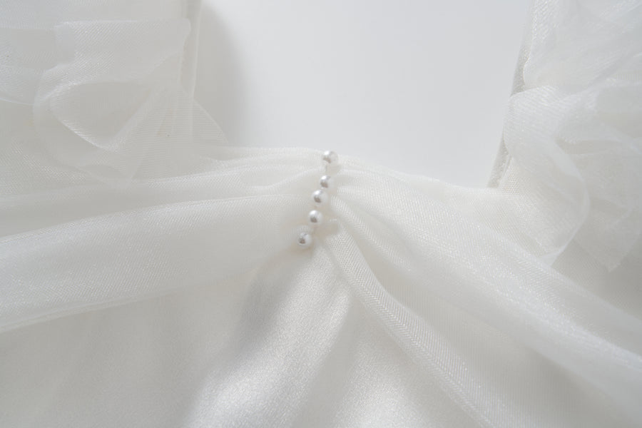 Close-up of the Cloud Whisper Dress by KIKI and JOJO, showcasing sheer white tulle and five pearl-like buttons arranged vertically at the center front.