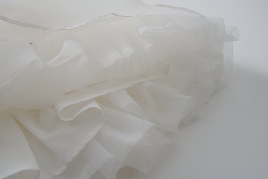 Close-up of the Ballerina Whisper Dress by KIKI and JOJO, showcasing layered white sheer fabric with ruffled edges, evoking a ballet-inspired, soft and airy texture against a plain background.