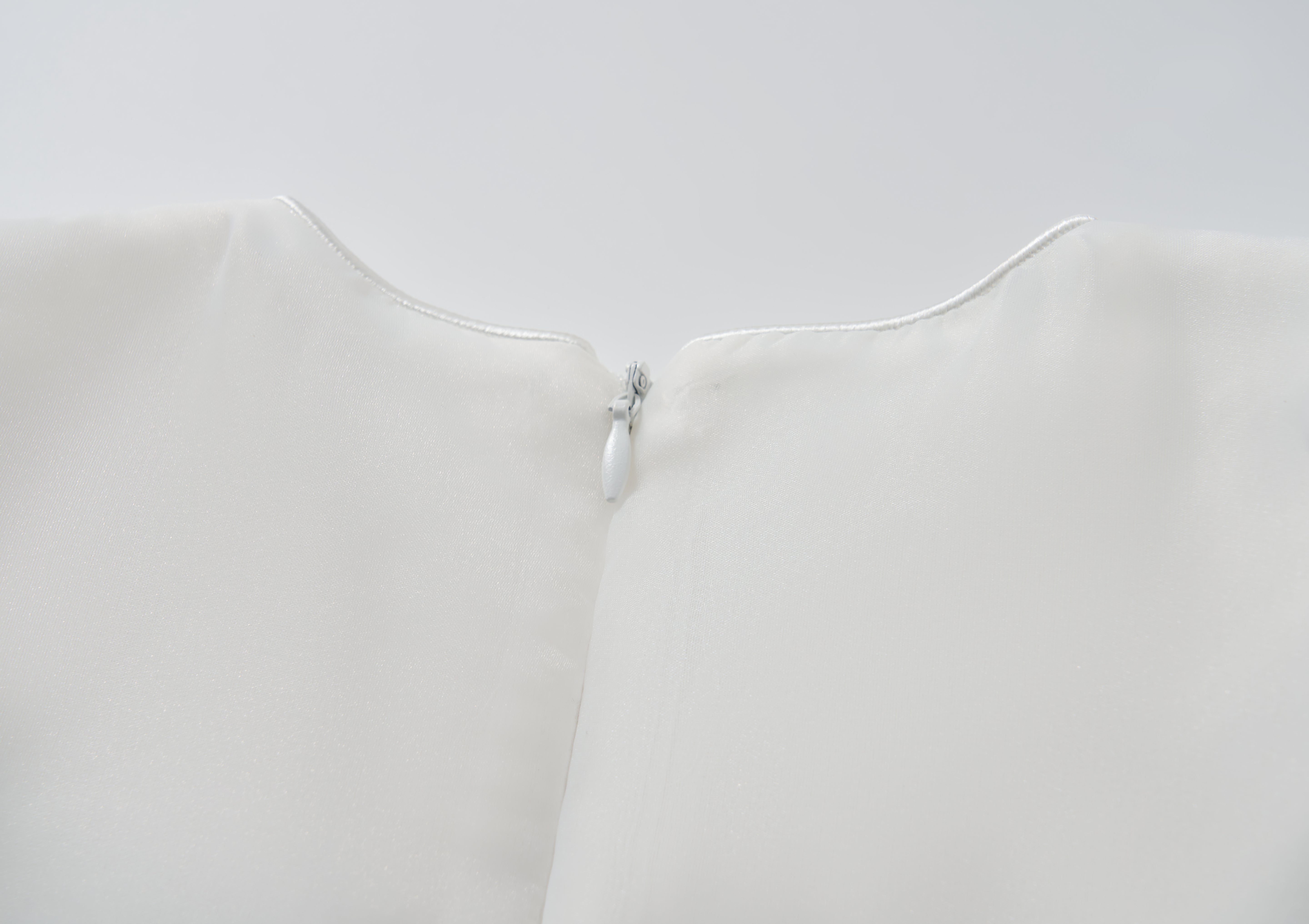 Close-up of the back neckline of the KIKI and JOJO Ballerina Whisper Dress in white, showing a small white zipper partially closed at the top.