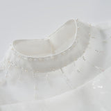 Close-up of the Whisper Bloom Dress by KIKI and JOJO, featuring a white high collar with bead and pearl accents in a radial neckline pattern. Subtle puff sleeves enhance the dress's elegant and sophisticated look.
