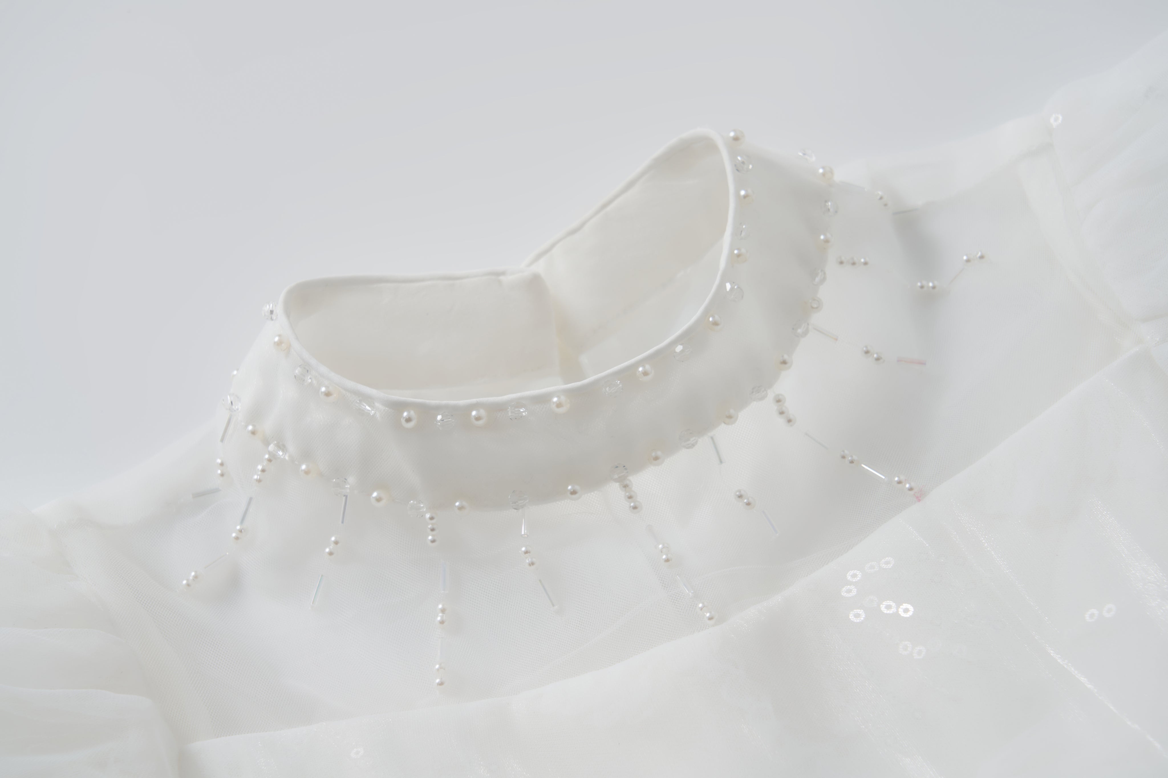 Close-up of the Whisper Bloom Dress by KIKI and JOJO, featuring a white high collar with bead and pearl accents in a radial neckline pattern. Subtle puff sleeves enhance the dress's elegant and sophisticated look.