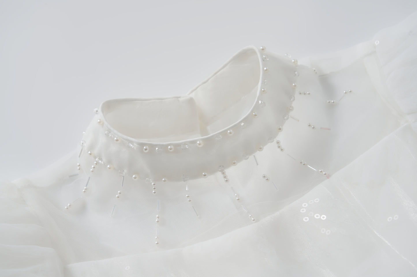 Close-up of the Whisper Bloom Dress by KIKI and JOJO, featuring a white high collar with bead and pearl accents in a radial neckline pattern. Subtle puff sleeves enhance the dress's elegant and sophisticated look.