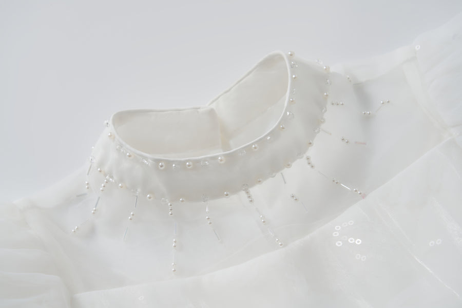 Close-up of the Whisper Bloom Dress by KIKI and JOJO, featuring a white high collar with bead and pearl accents in a radial neckline pattern. Subtle puff sleeves enhance the dress's elegant and sophisticated look.