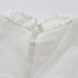 Close-up of the Whisper Bloom Dress by KIKI and JOJO, showing its white sheer collar adorned with pearls, sequins, beads, and finished with a single button at the neckline.