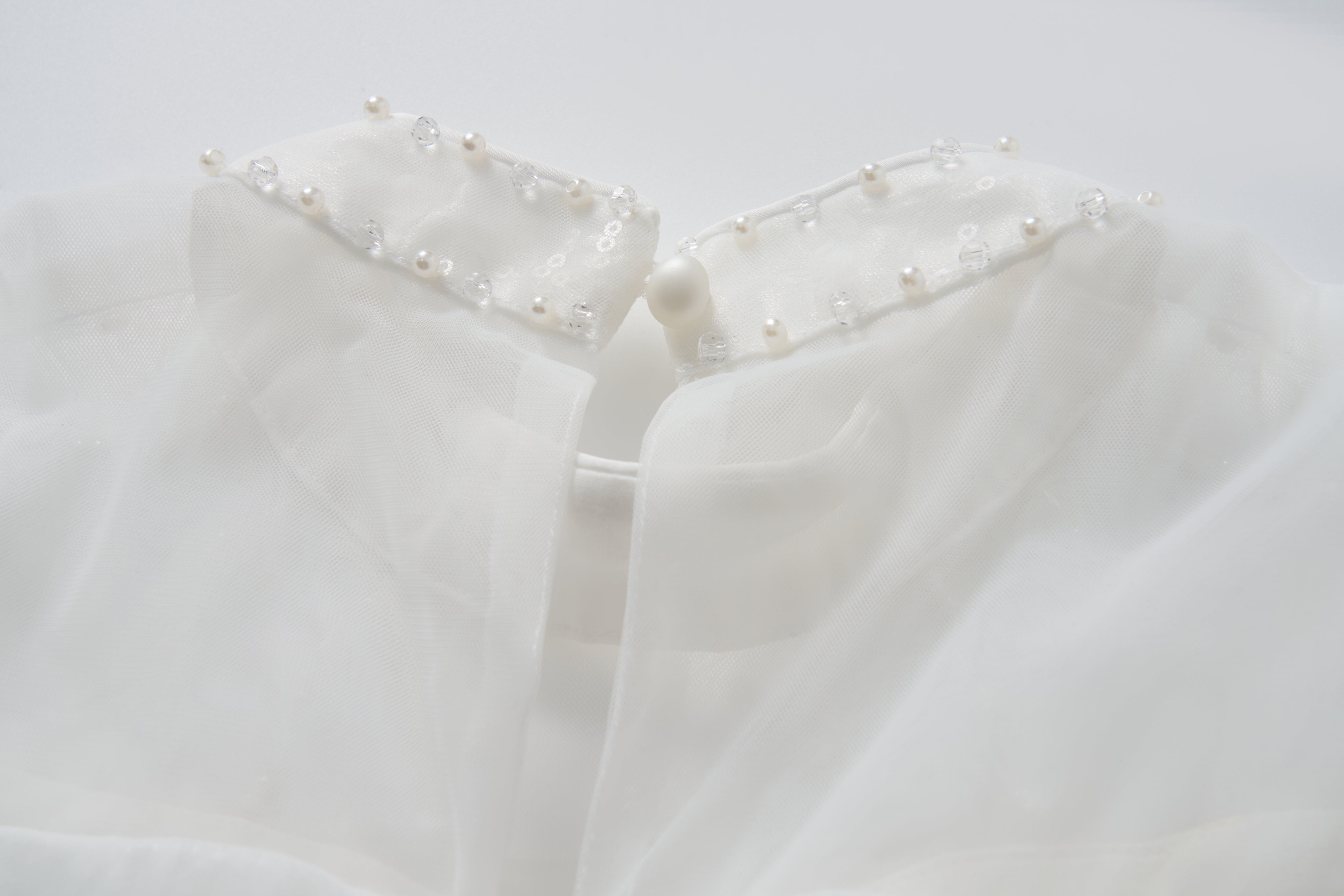 Close-up of the Whisper Bloom Dress by KIKI and JOJO, showing its white sheer collar adorned with pearls, sequins, beads, and finished with a single button at the neckline.