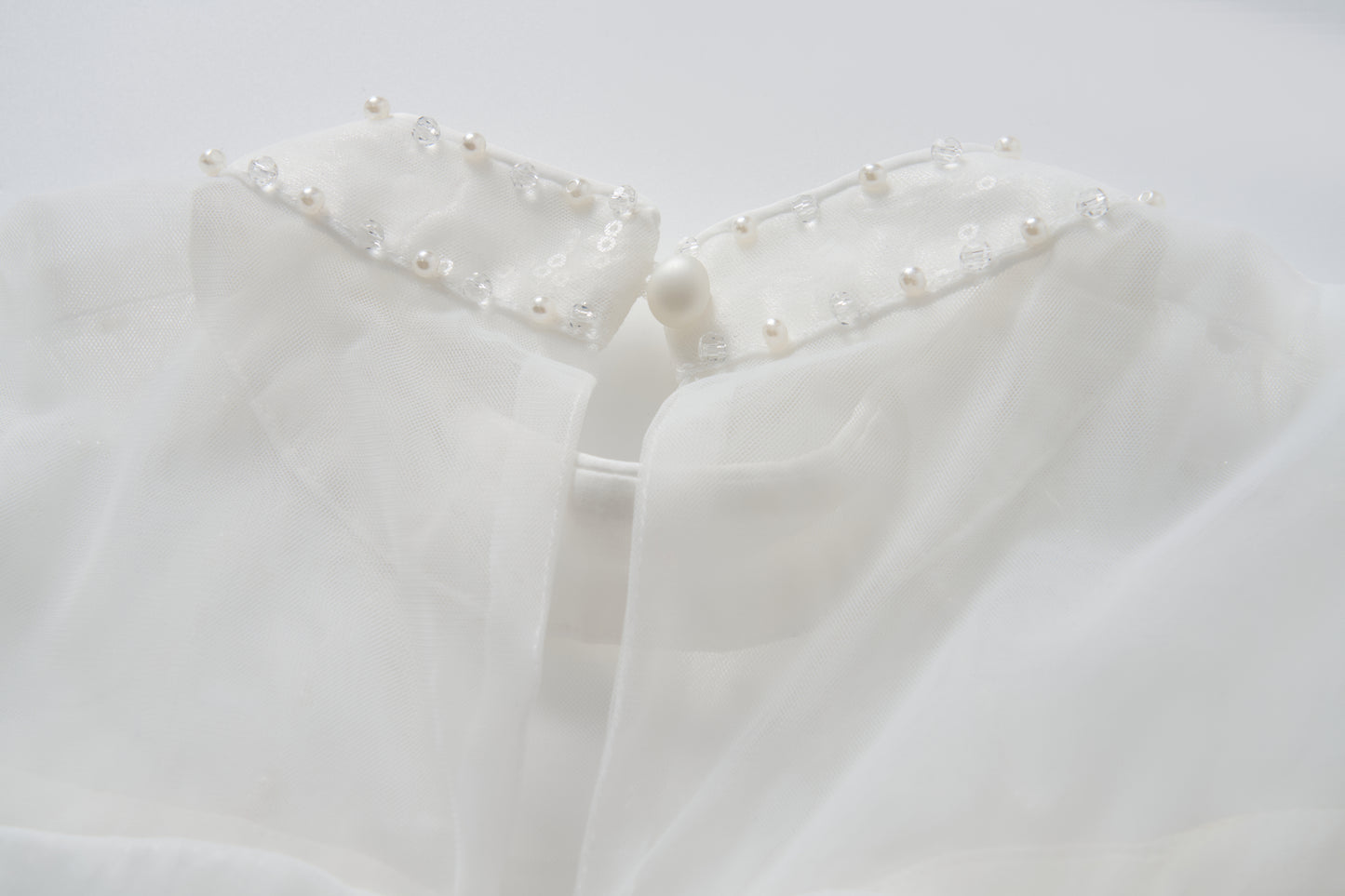 Close-up of the Whisper Bloom Dress by KIKI and JOJO, showing its white sheer collar adorned with pearls, sequins, beads, and finished with a single button at the neckline.