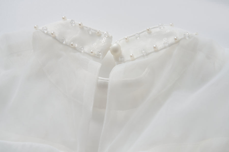 Close-up of the Whisper Bloom Dress by KIKI and JOJO, showing its white sheer collar adorned with pearls, sequins, beads, and finished with a single button at the neckline.