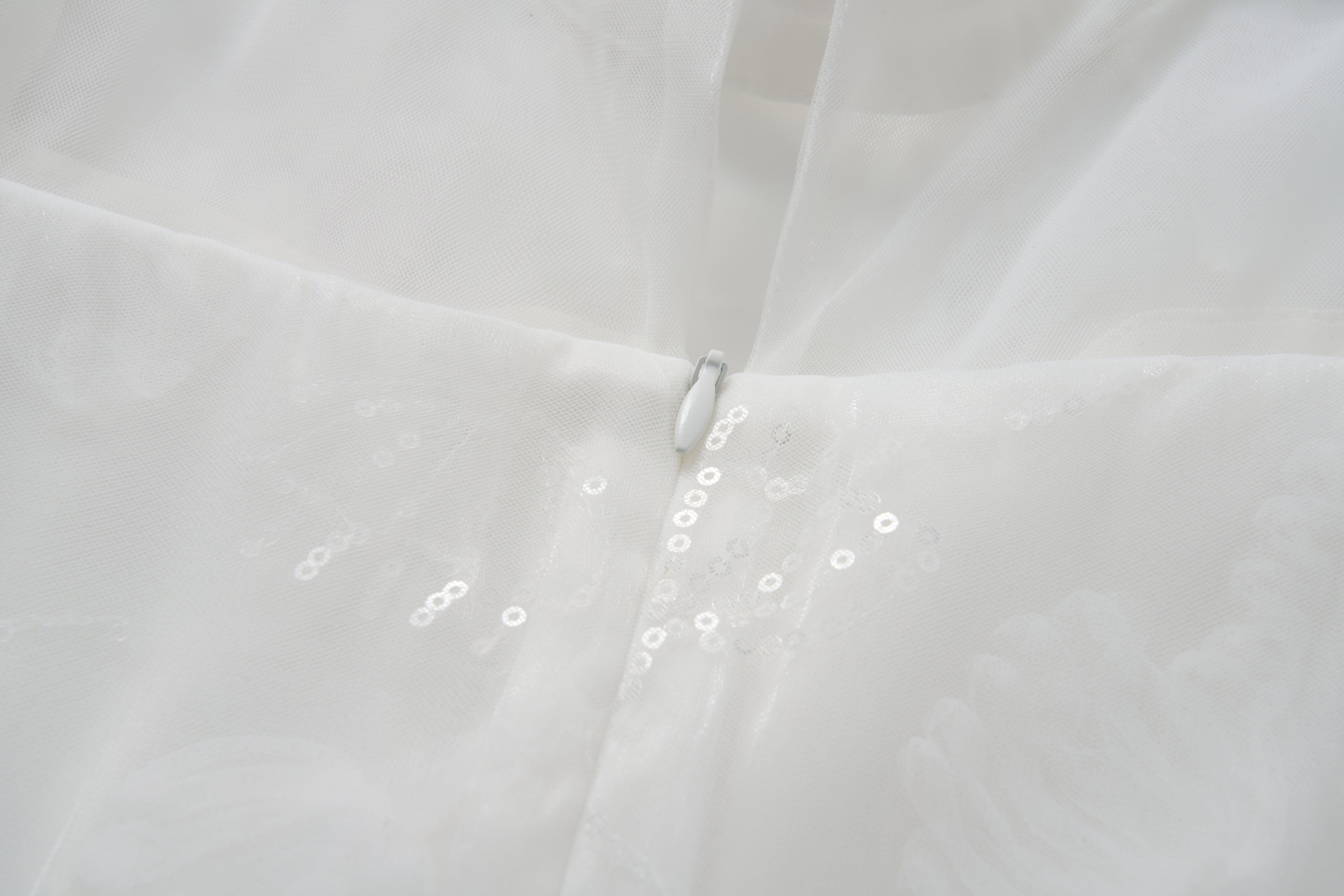 Close-up of the Whisper Bloom Dress by KIKI and JOJO—a white mini dress with floral embroidery, zipper closure, sheer fabric adorned with subtle sequins, and delicate bead accents.