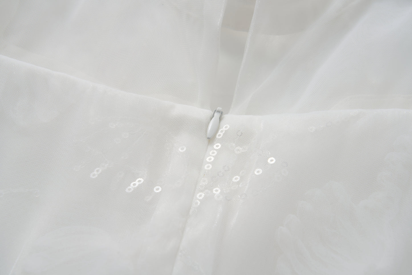 Close-up of the Whisper Bloom Dress by KIKI and JOJO—a white mini dress with floral embroidery, zipper closure, sheer fabric adorned with subtle sequins, and delicate bead accents.