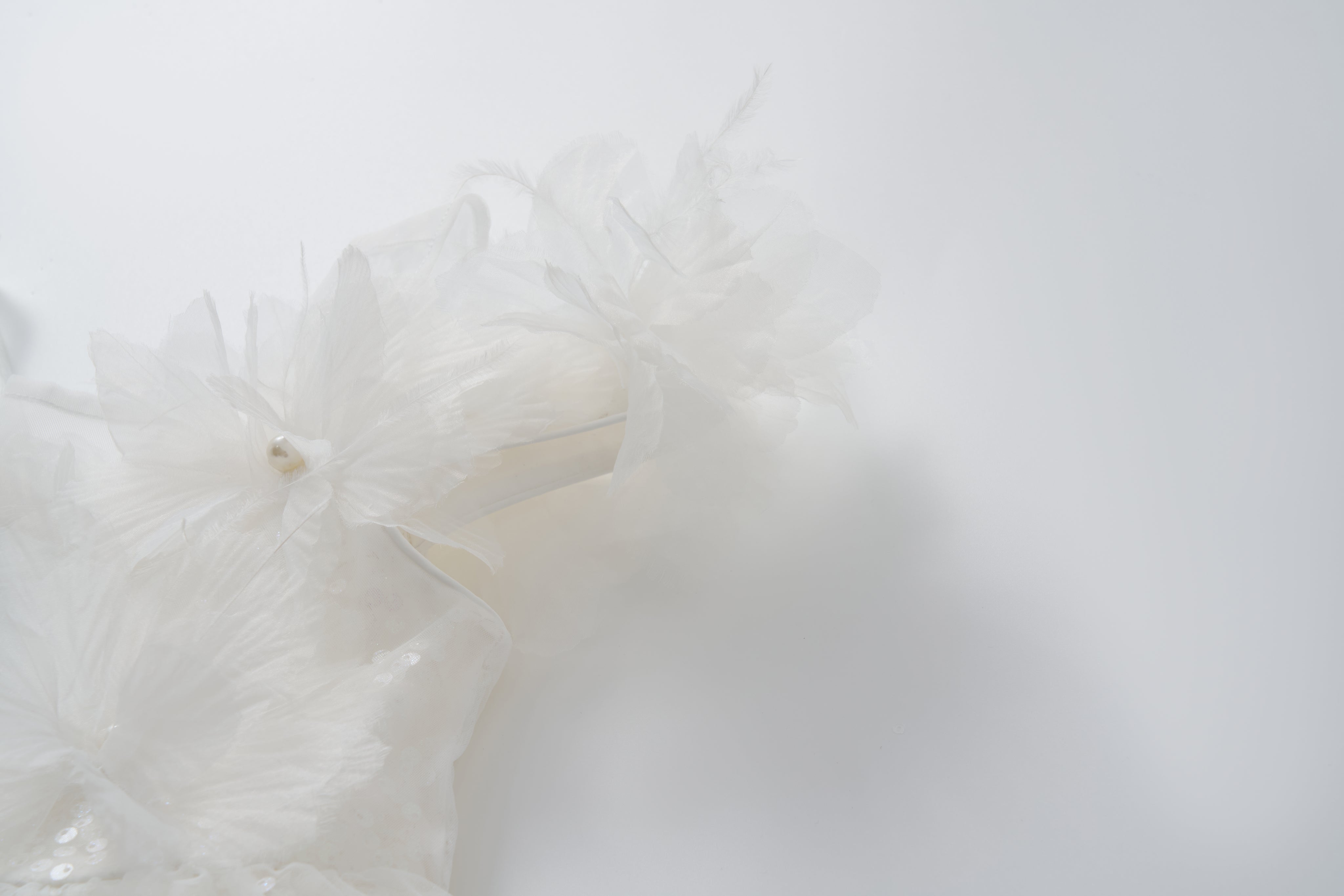Close-up of the Feathered Whisper Dress by KIKI and JOJO, featuring delicate white fabric with translucent, layered floral accents—evoking a soft, ethereal look against a plain white background.
