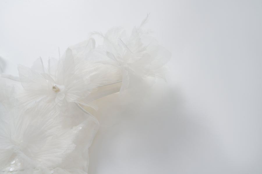 Close-up of the Feathered Whisper Dress by KIKI and JOJO, featuring delicate white fabric with translucent, layered floral accents—evoking a soft, ethereal look against a plain white background.