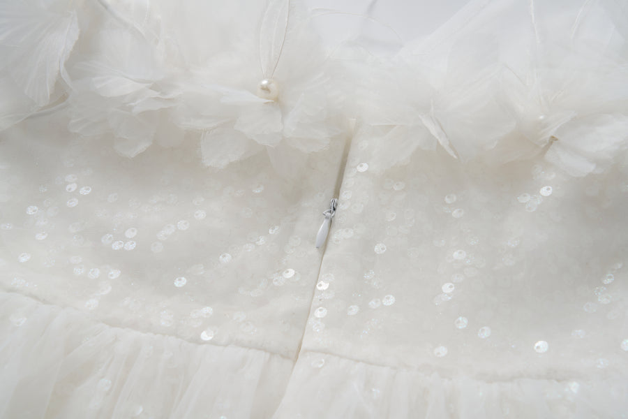 Close-up of the Feathered Whisper Dress by KIKI and JOJO—a white sequined fabric with floral tulle, pearl accents, and a hidden center zipper—ideal for an off-shoulder A-line silhouette.