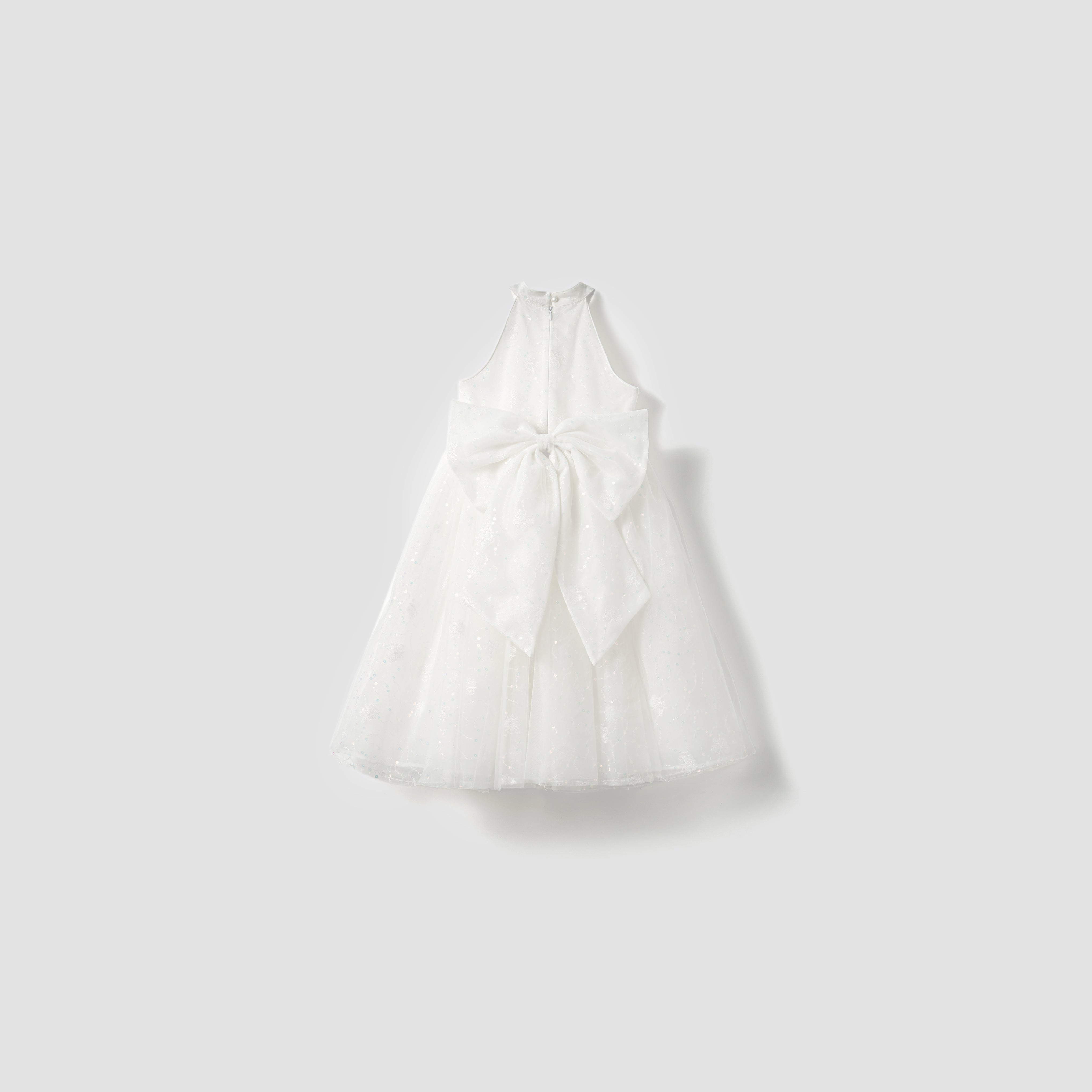 The Butterfly Whispers Dress by KIKI and JOJO is a white satin A-line halter dress with a large back bow, displayed on a plain light gray background. Its unique design and flattering silhouette exude elegant charm.