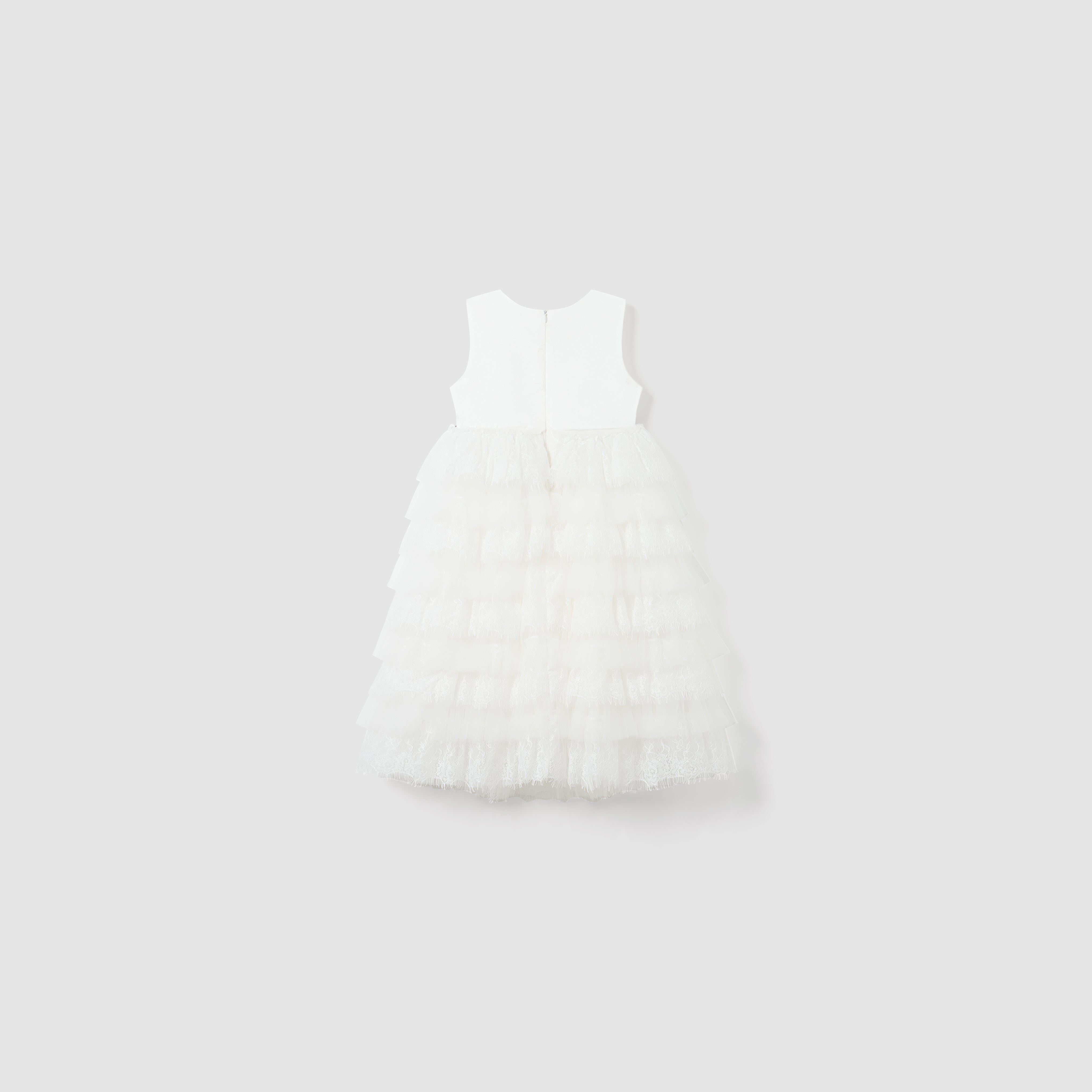 The Monochrome Whisper Dress by KIKI and JOJO features a sleeveless white lace ruffle design, a fitted bodice, and a long tiered skirt, shown against a plain light gray background.