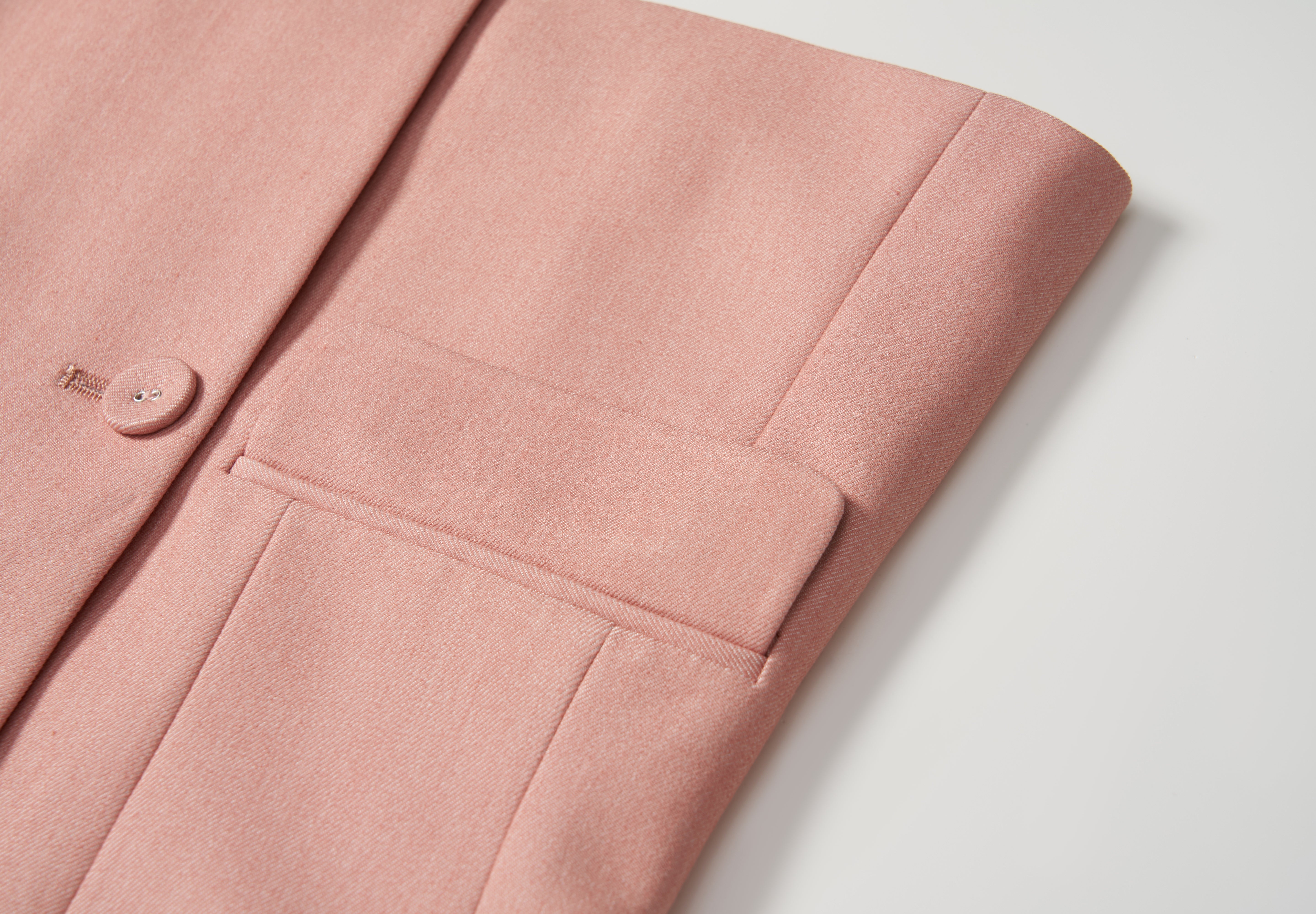 Close-up of the Blush Reverie Suit Jacket by KIKI and JOJO, showing the blush pink sleeve and pocket on a white surface, with focus on the button detail and fabric texture.