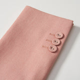 A pair of Blush Reverie Suit Pants by KIKI and JOJO, featuring an adjustable waistband and three matching buttons in a row, is displayed folded on a white surface.