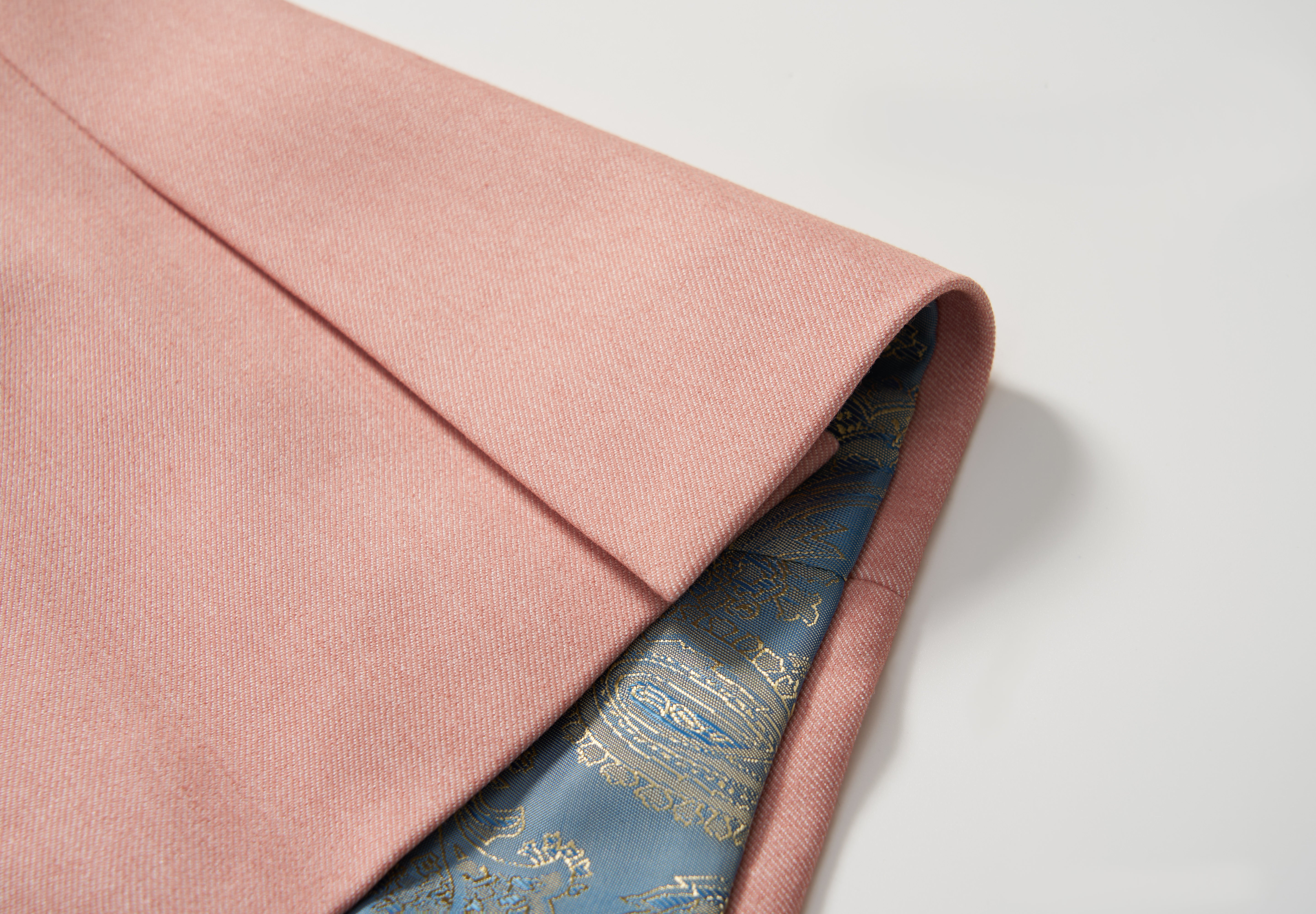 A close-up of the Blush Reverie Suit Jacket by KIKI and JOJO shows its folded blush pink exterior and striking blue silk lining with a gold paisley pattern, making it perfect for any boy’s special occasion.
