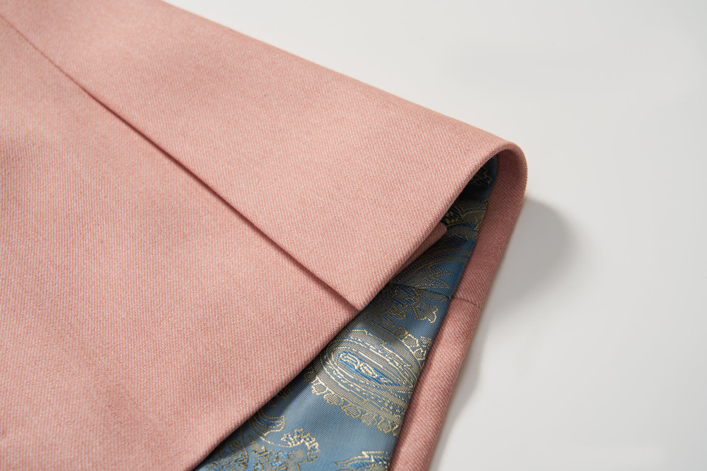 A close-up of the Blush Reverie Suit Jacket by KIKI and JOJO shows its folded blush pink exterior and striking blue silk lining with a gold paisley pattern, making it perfect for any boy’s special occasion.