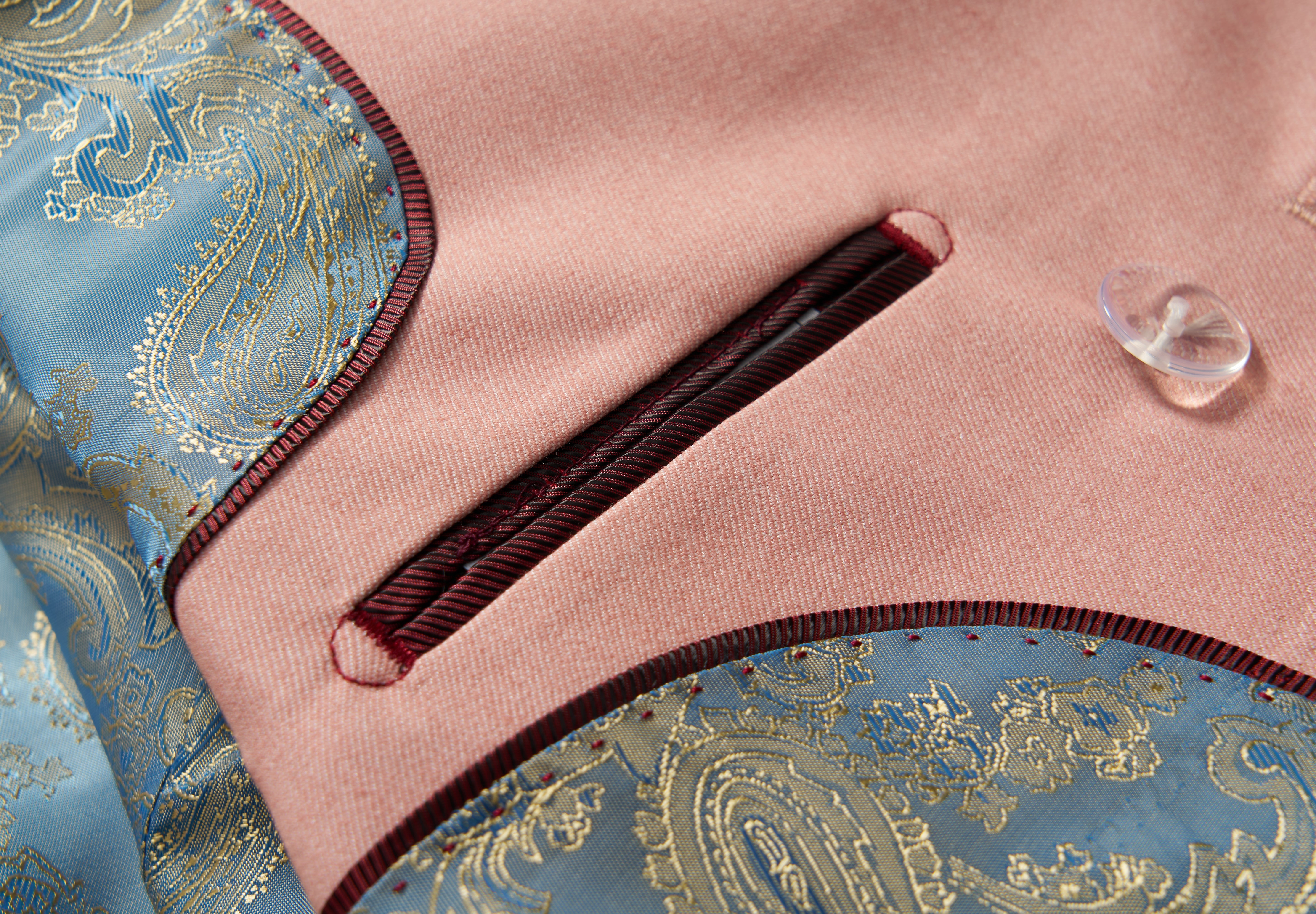 Close-up of the KIKI and JOJO Blush Reverie Suit Jacket, featuring a blush pink hue, burgundy-trimmed pocket, blue and gold paisley accents, and a translucent button—ideal for boys' special occasions.