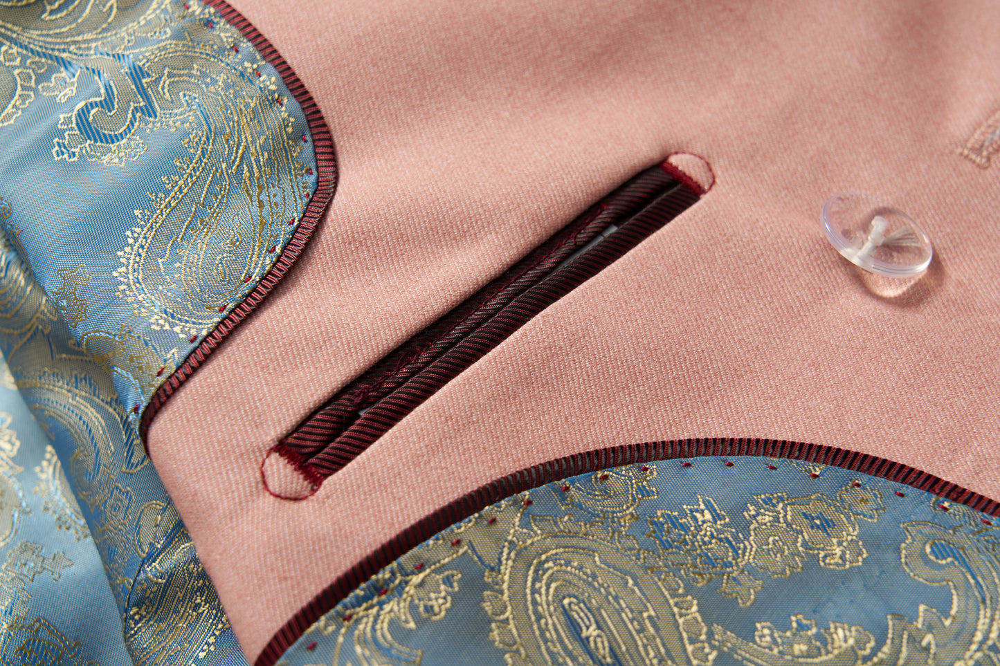 Close-up of the KIKI and JOJO Blush Reverie Suit Jacket, featuring a blush pink hue, burgundy-trimmed pocket, blue and gold paisley accents, and a translucent button—ideal for boys' special occasions.
