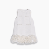 The KIKI and JOJO Girls Elegance A-Line Chiffon Trim Dress in Champagne features a sleeveless design, textured fabric, front decorative pockets, and delicate ruffled chiffon trim at the hem.
