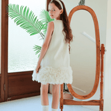 A young girl wears the KIKI and JOJO Girls Elegance A-Line Chiffon Trim Dress in Champagne with a headband, standing by a full-length mirror in a bright room with potted plants.