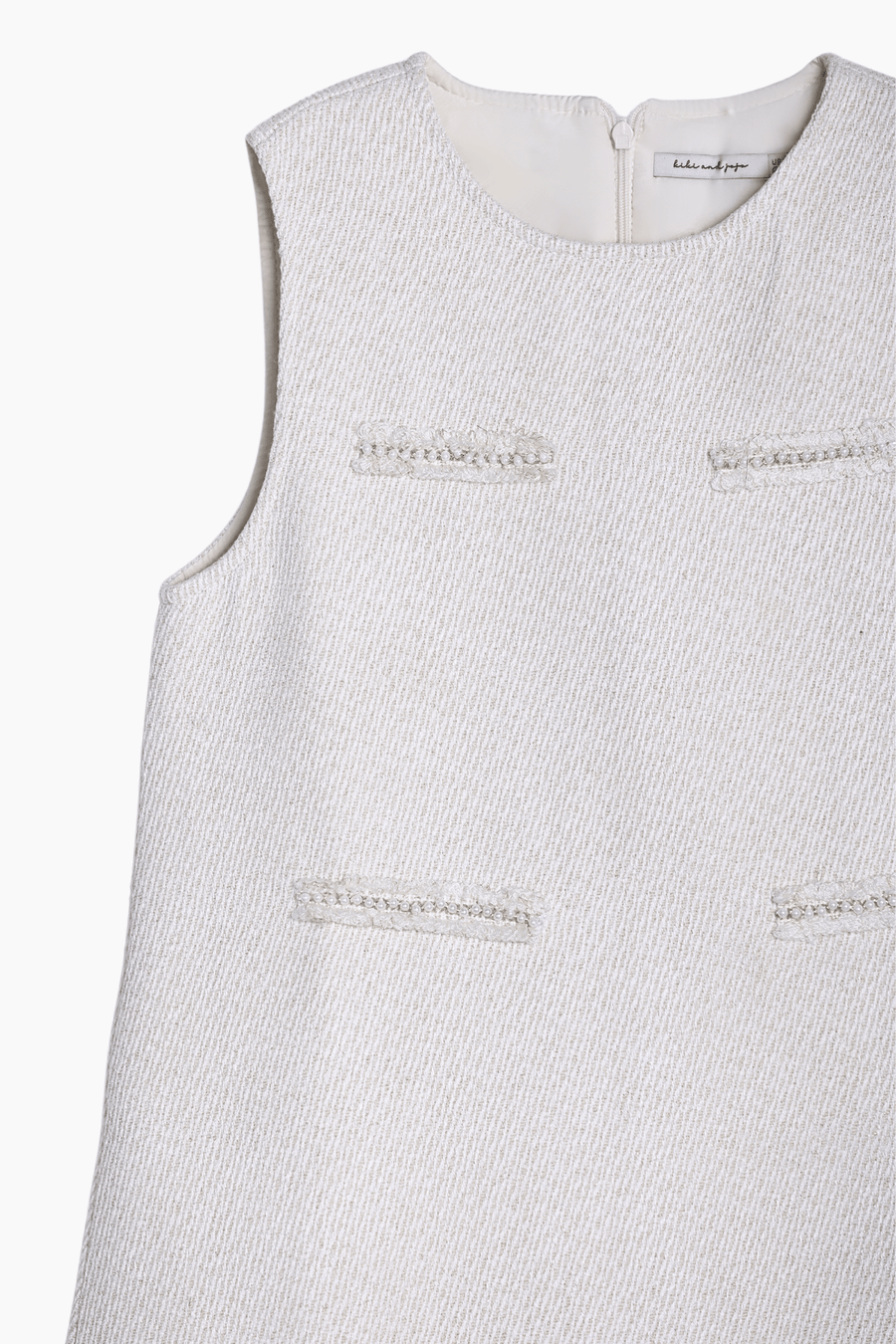 The KIKI and JOJO Girls Elegance A-Line Chiffon Trim Dress in champagne features a sleeveless, textured design with four decorative front details and a back zipper closure.
