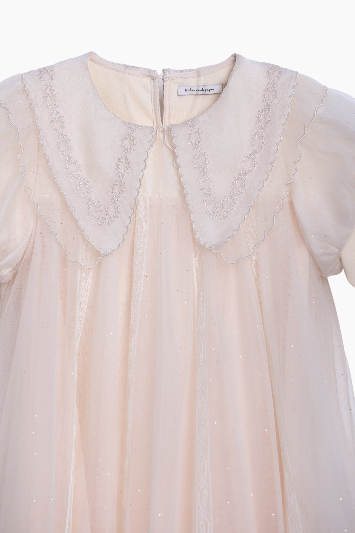 The KIKI and JOJO Girls Embroidered Satin Collar Sparkle Tulle Dress in Beige/Ivory features a sheer overlay, puffed short sleeves, a scalloped embroidered satin collar, and a back zipper.