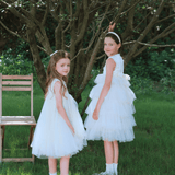 Two young girls in KIKI and JOJO's Girls Embroidered Satin & Tulle Dress - Ivory stand on grass near a wooden chair and tree; one faces forward while the other makes a peace sign—a perfect special occasion moment.