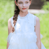 A young girl with a braid and headband wears the KIKI and JOJO Girls Embroidered Satin & Tulle Dress in ivory, ideal for special occasions, standing outdoors in natural light.