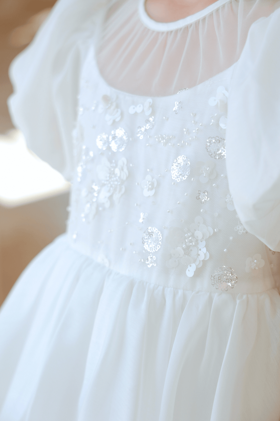 Close-up of the KIKI and JOJO Girls Pearl-Embroidered Satin Dress in Pure White, showcasing a sheer neckline, puffy sleeves, floral sequin details, and delicate hand-embroidered pearl accents.