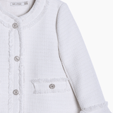 The Girls Pearlescent Elegance Tweed Jacket in Soft Champagne by KIKI and JOJO features a finely woven texture, pearl-like buttons, a round collar, front pockets, and frayed edges for timeless style.