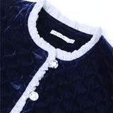 Close-up of the KIKI and JOJO Girls Quilted Ruffle Jacket in Sapphire Blue, featuring diamond-quilted velvet, clear petal-shaped buttons, and a light gray ruffled collar trim.