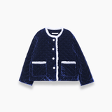 The KIKI and JOJO Girls Quilted Ruffle Jacket in Sapphire Blue features a diamond-quilted design, white trim, petal-shaped buttons, and two front pockets, shown on a plain white background.