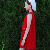 A young person in the KIKI and JOJO Girls Tweed Dress in cranberry red and a white beret stands in profile against green bushes.