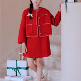 A girl wearing the KIKI and JOJO Girls Tweed Jacket in Cranberry Red with champagne gold buttons stands on a staircase beside wrapped gifts, holding the railing and looking at the camera.