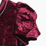 Close-up of the KIKI and JOJO Girls Velvet Puff Sleeve Dress in burgundy red, featuring rhinestone trim—an elegant choice for special occasions—shown against a white background.