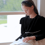 A girl in the KIKI and JOJO Girls Velvet & Tulle Sparkle Dress - Black/Ivory sits by a window, pearl headband in her hair, reading an open book as gentle daylight fills the room.
