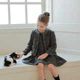 A young girl in a KIKI and JOJO Girls Vintage Beaded Tweed Jacket - Gray sits on a windowsill, gently reaching out to touch a small black and white kitten.