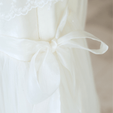Close-up of the KIKI and JOJO Girls Vintage Lace Satin & Tulle Dress in beige, featuring white lace details, satin tulle, and a sheer fabric bow at the waist.